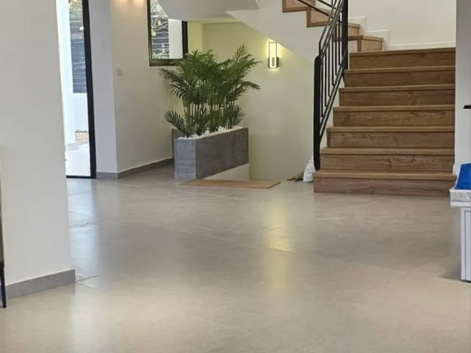 סלון מרווח אחרי שיפוץ עם גרם מדרגות, ריצוף בהיר וצמחייה
